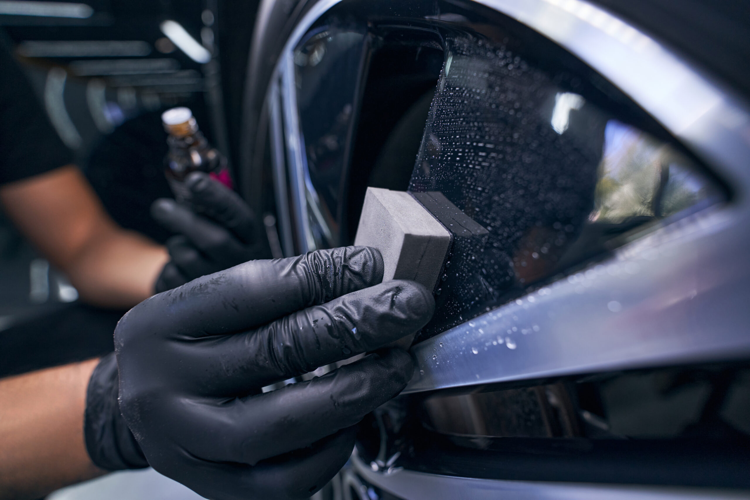 Professional applying ceramic coating to car window with applicator block