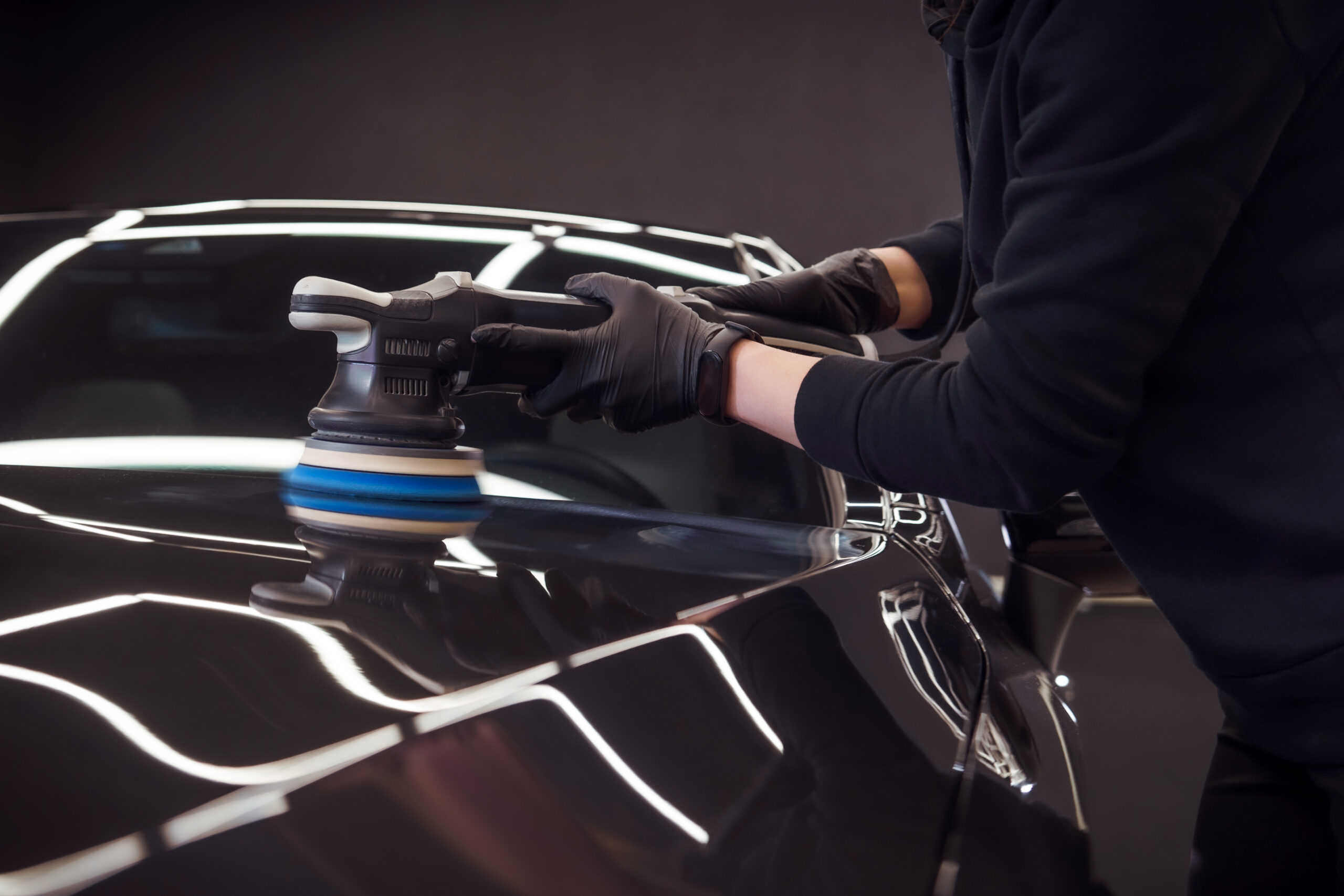 Professional detailer using orbital polisher on black car paint