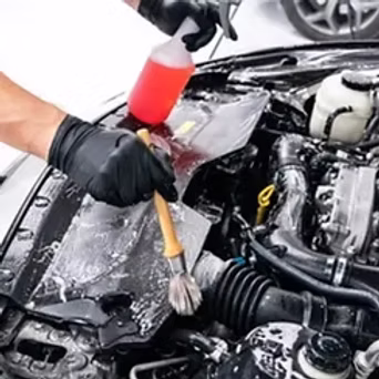 Technician cleaning car engine bay with red brush and soap solution