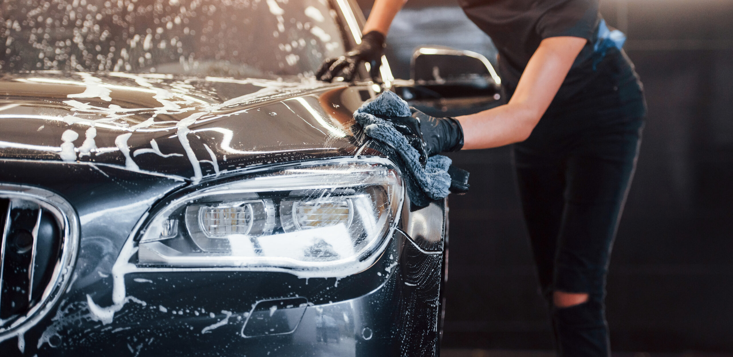 Professional hand washing black car with soapy water and microfiber mitt