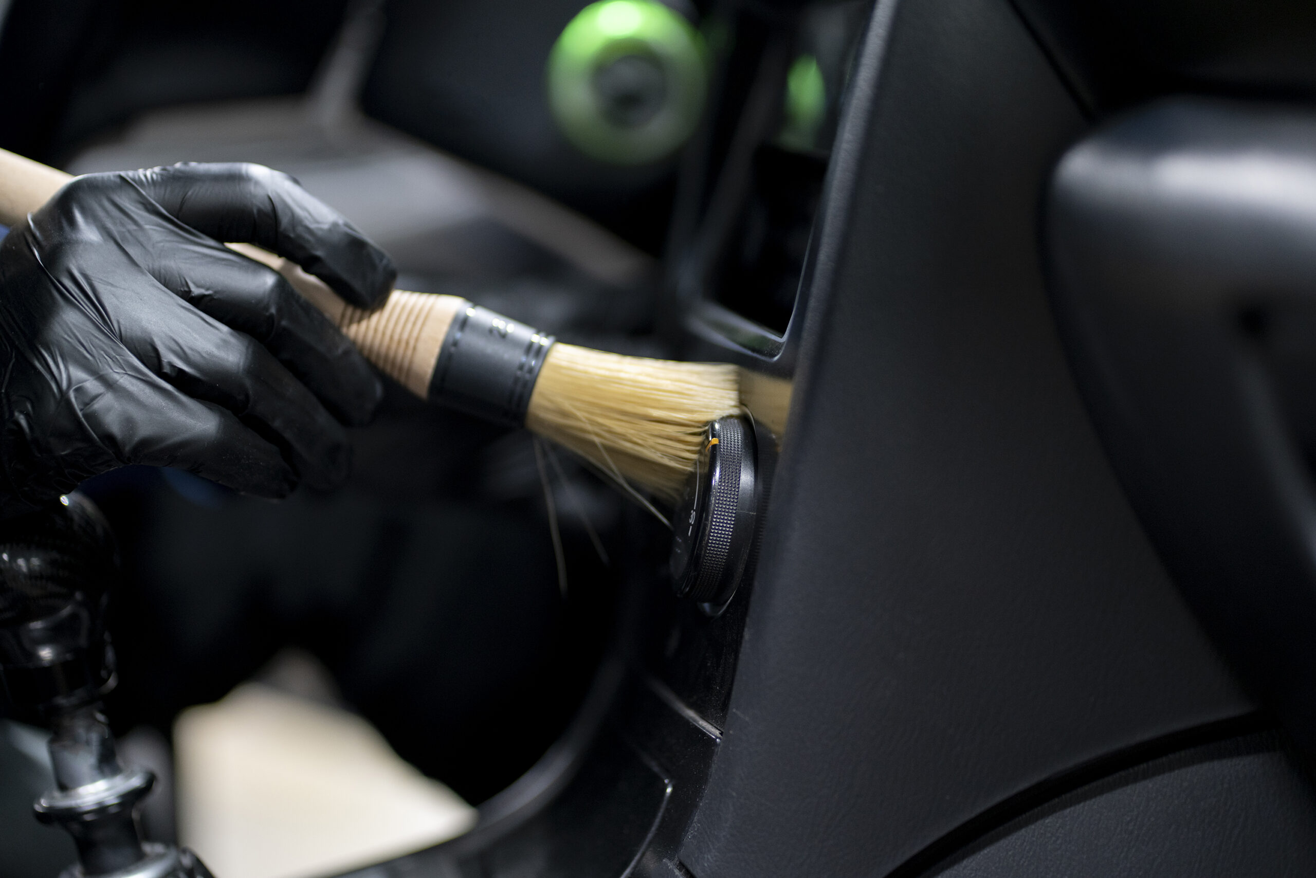 Professional detailer cleaning car interior with brush wearing black gloves