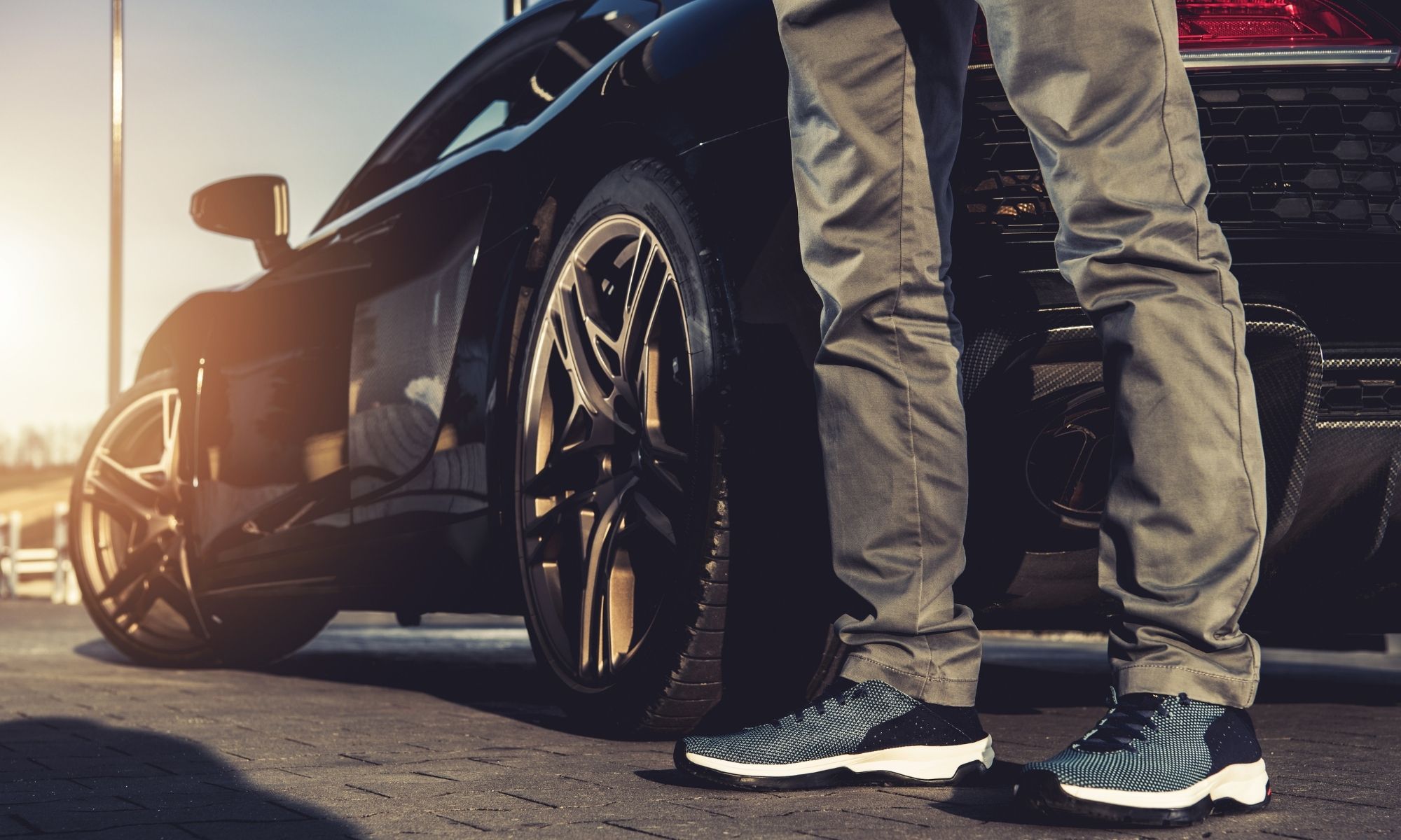 Man standing beside luxury black car with polished gold wheels