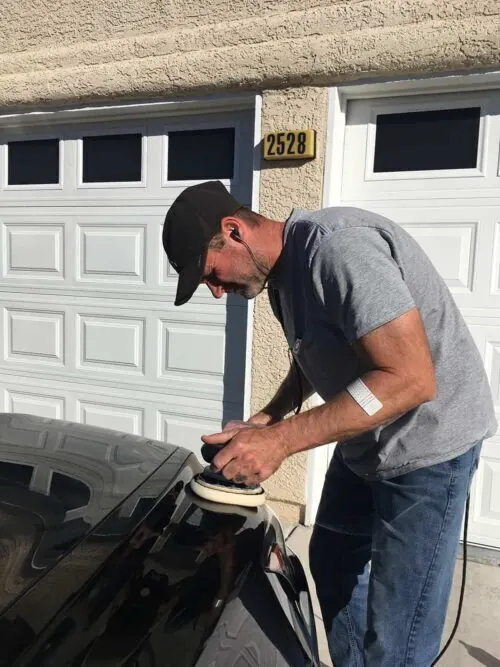 Professional auto detailer using machine polisher on black vehicle